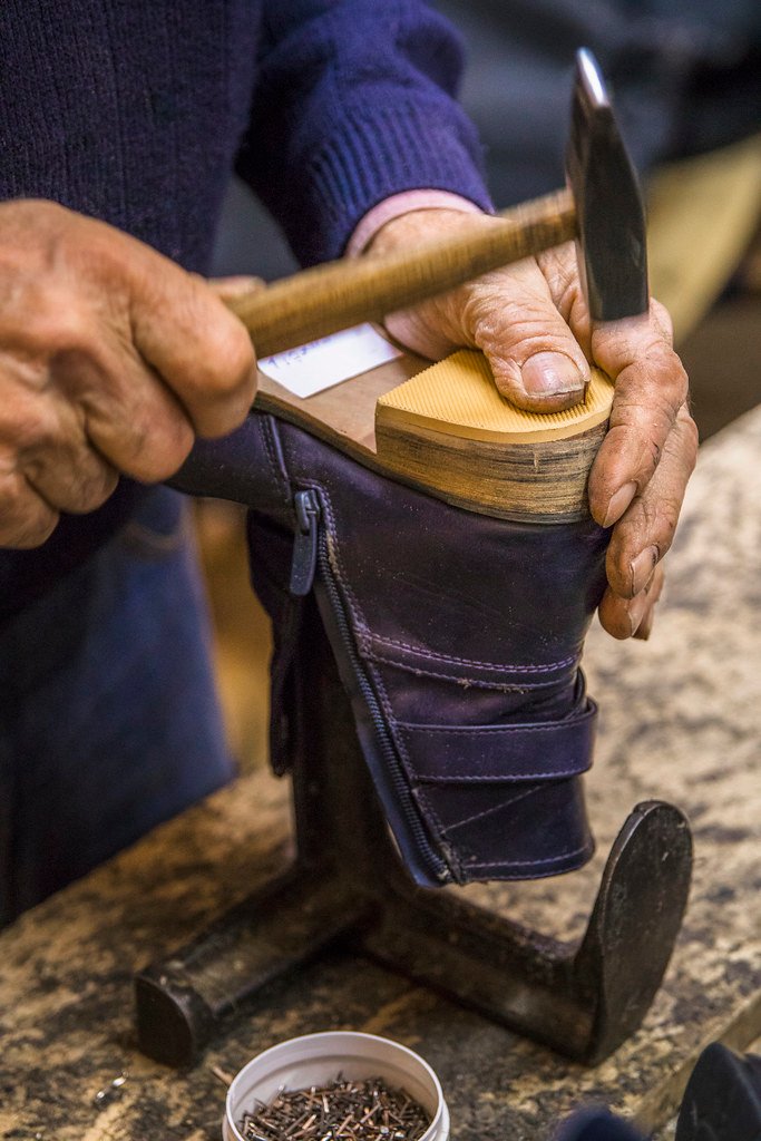 Shoe repairman nailing a new heel on a boot. Resoling