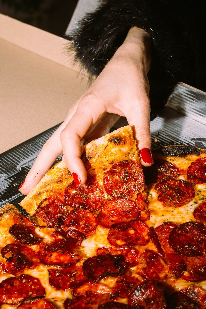 A well-manicured hand with red nails reaches for a slice of delicious pepperoni pizza