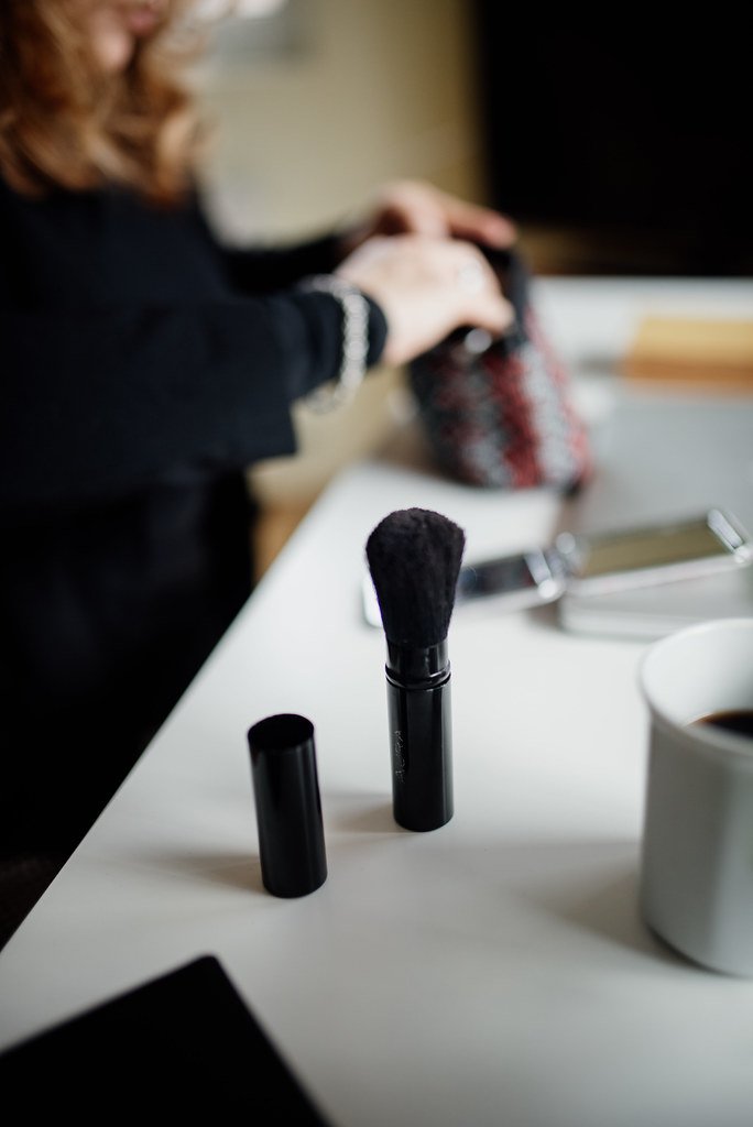 Applying makeup with a brush on a table while preparing for a day out in a cozy indoor environment