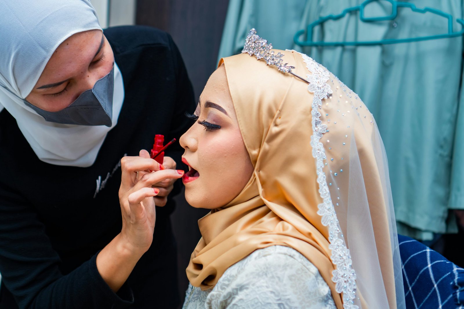 a woman in a hijab is putting lipstick on another woman's lips