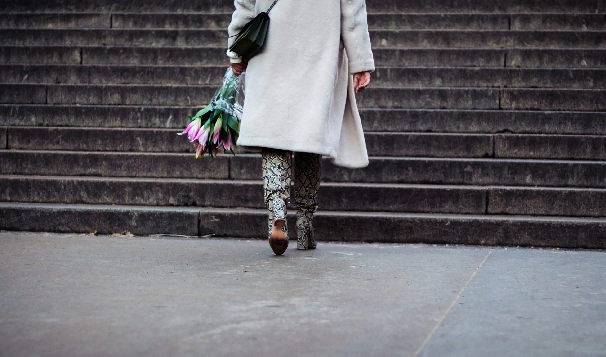 a woman walking down a street holding a bunch of flowers