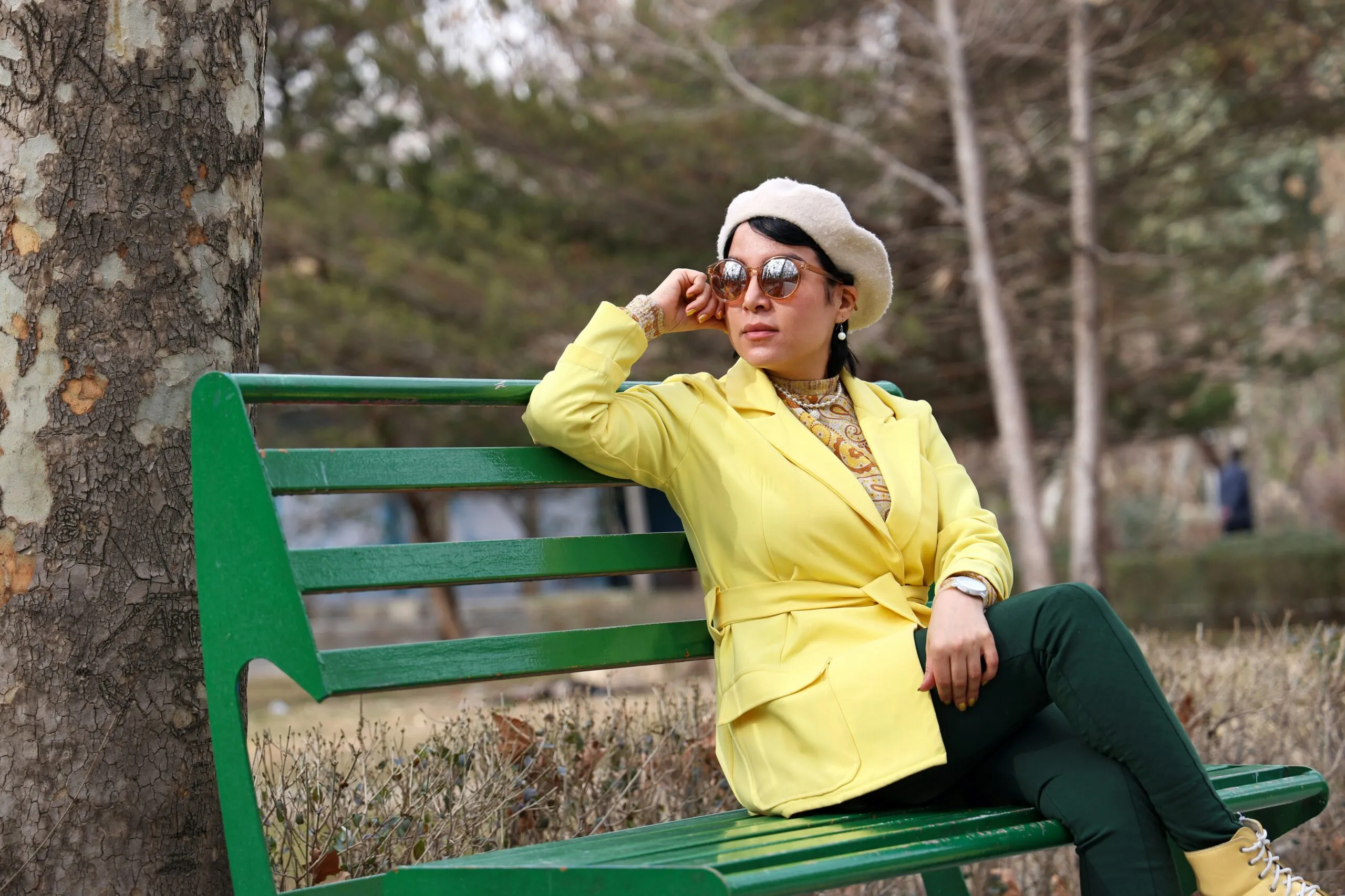 Woman in yellow jacket sits on a park bench
