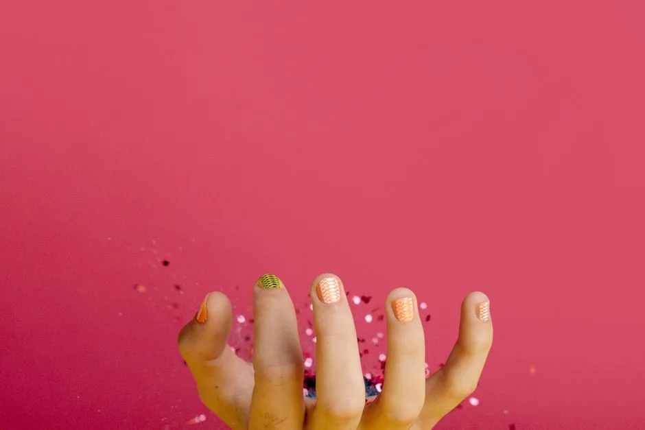 Detailed view of a hand showcasing colorful manicure against a vibrant pink backdrop, offering ample copy space.