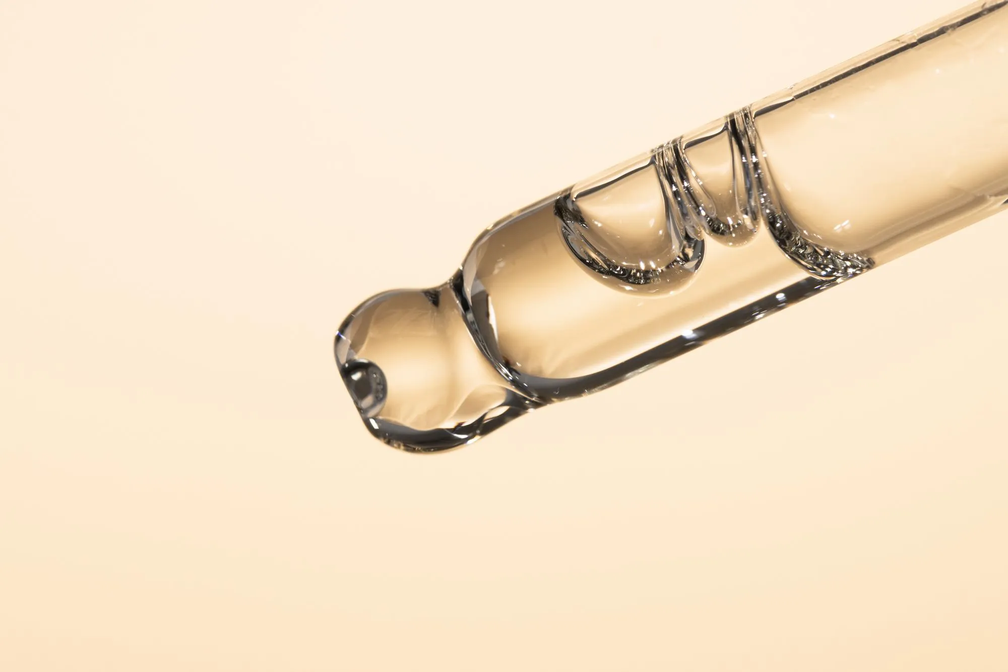 Closeup of a glass dropper with transparent cosmetic oil peptide serum on a beige background