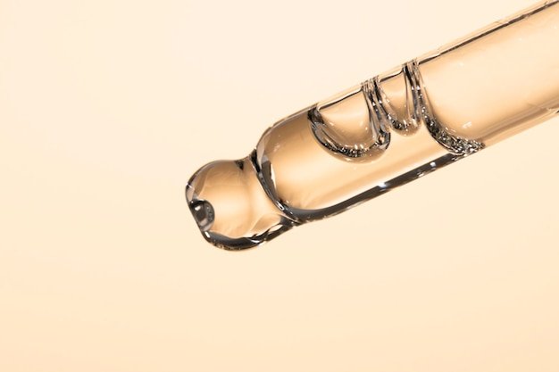 Closeup of a glass dropper with transparent cosmetic oil peptide serum on a beige background