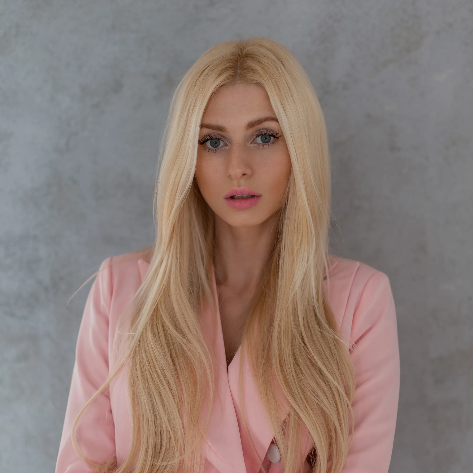 Fashion pretty attractive girl woman in a glamorous stylish pink suit stands near the gray wall