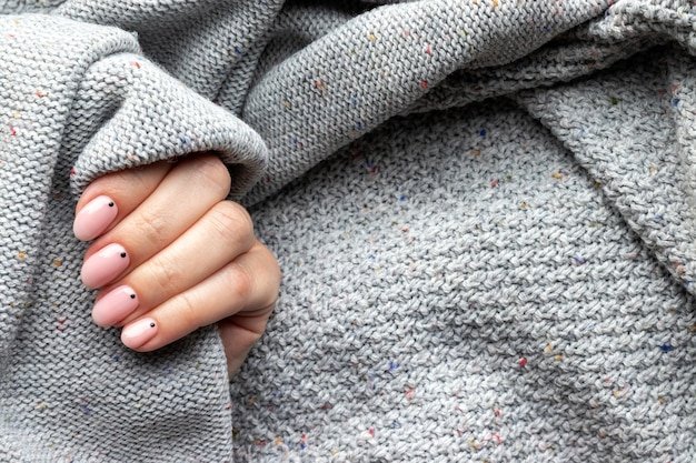 Female hand in a gray knitted sweater fabric with trendy beautiful manicure