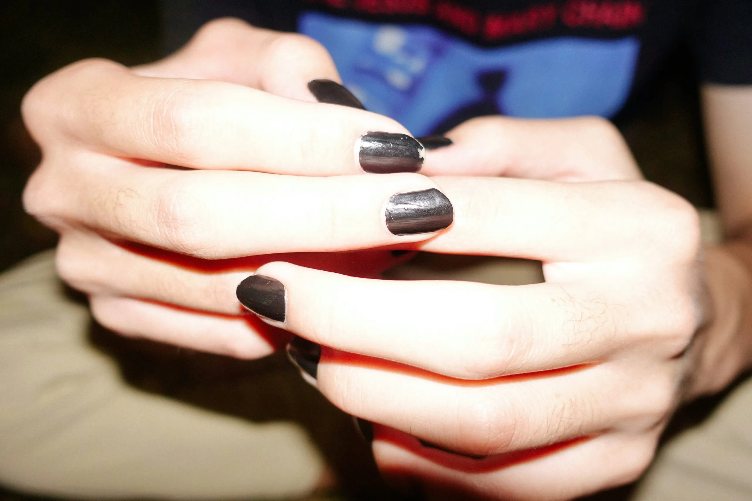Hands are clasped, showcasing black nail polish.