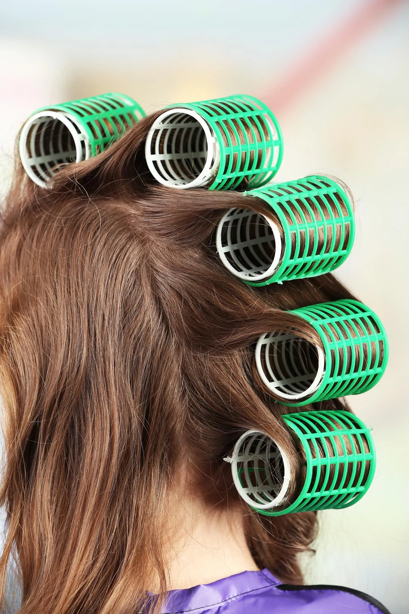 Long female hair during hair dressing with curler closeup on light background