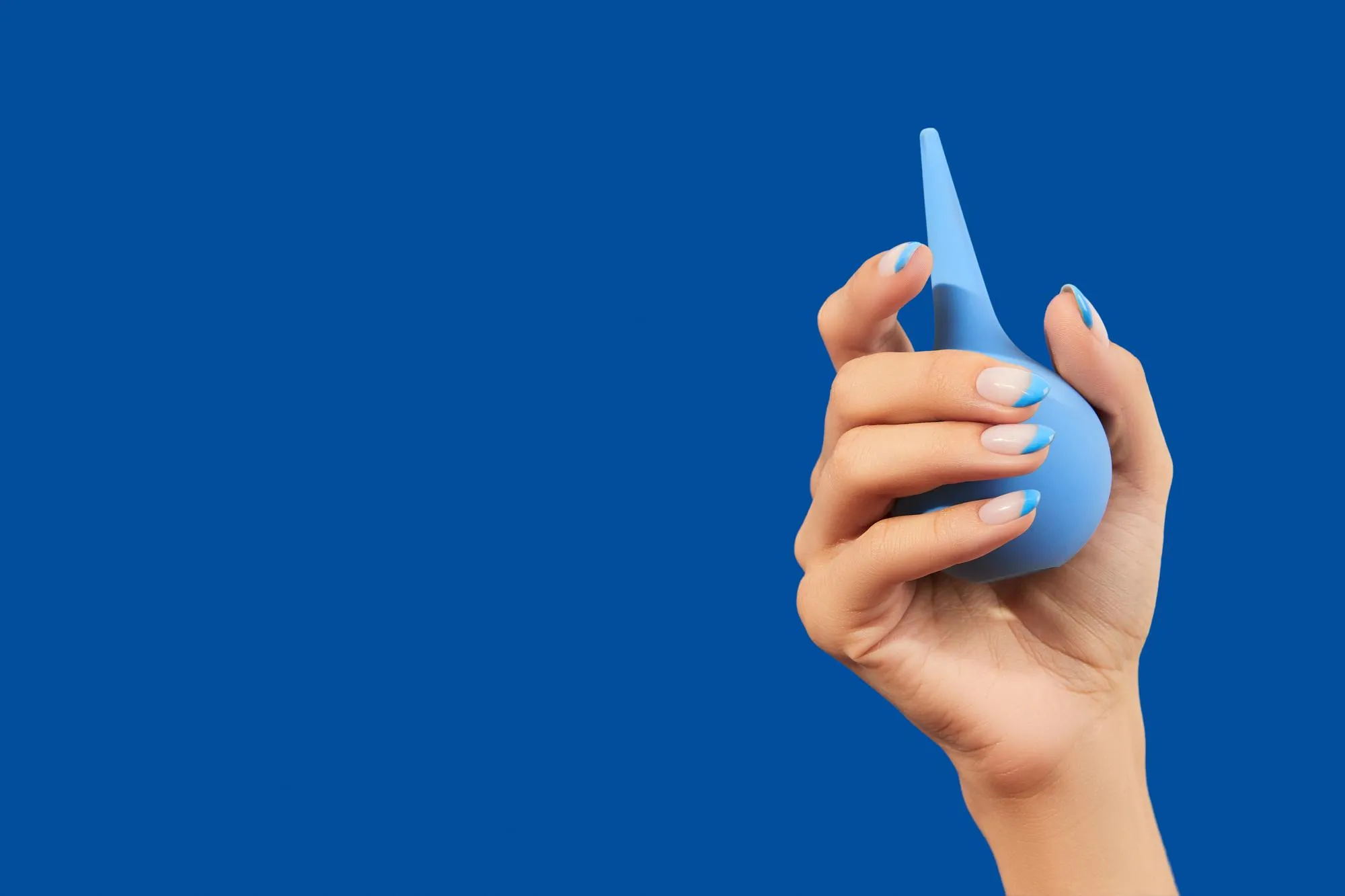 Wellgroomed womans hand holding enema on blue background