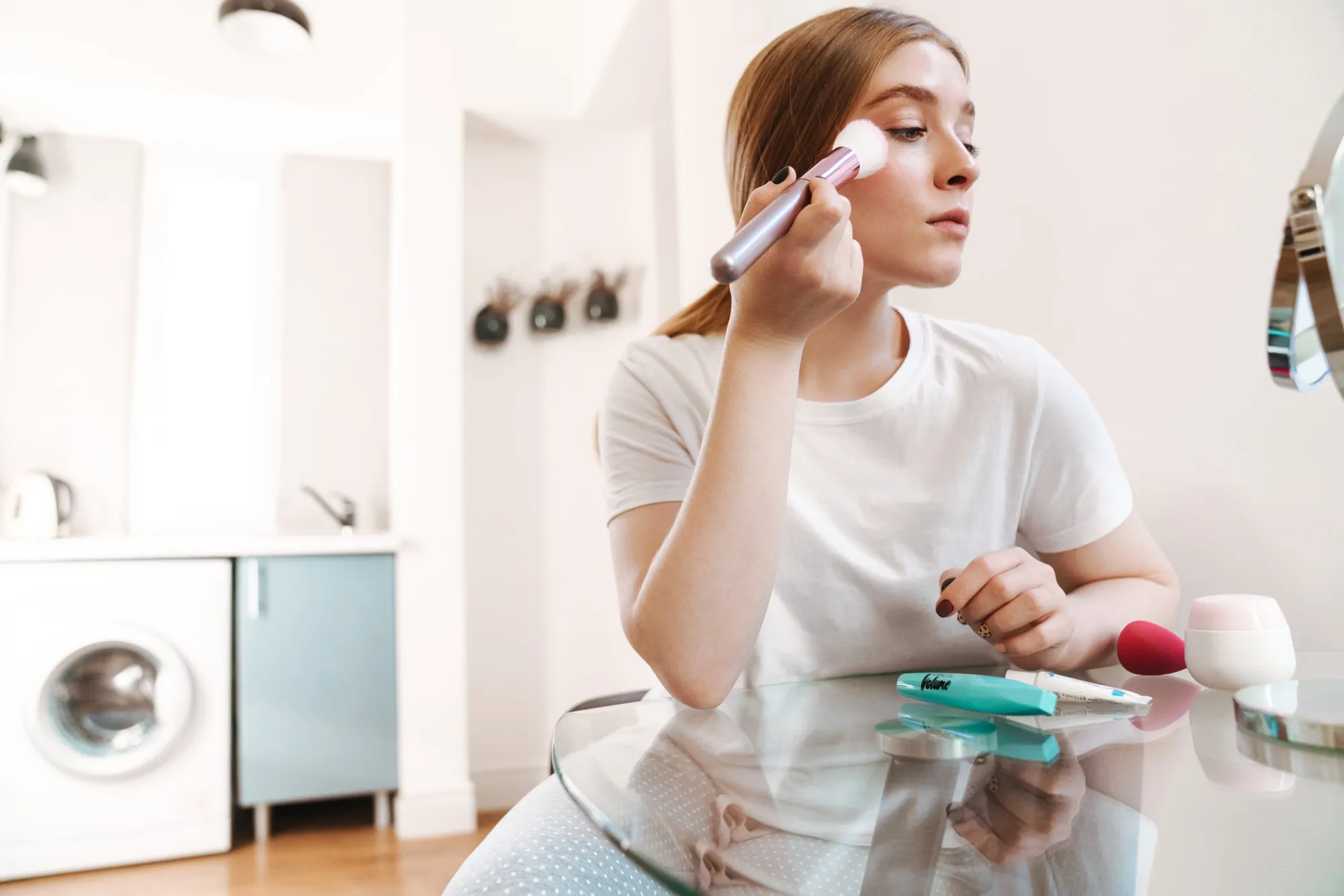 young amazing concentrated girl indoors at home in bedroom on bed with mirror apply makeup.