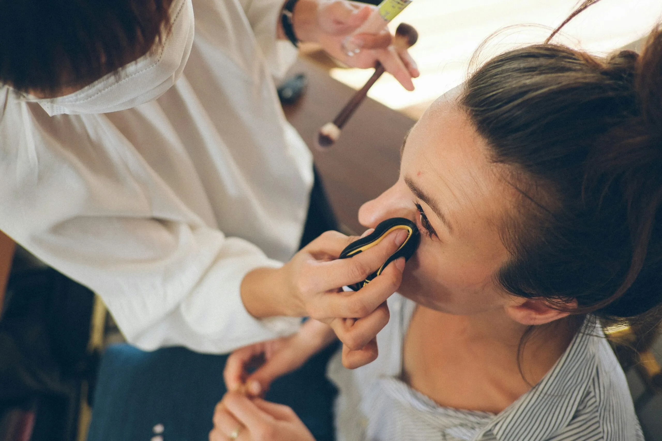 Makeup artist applying eye shadow to a woman.
