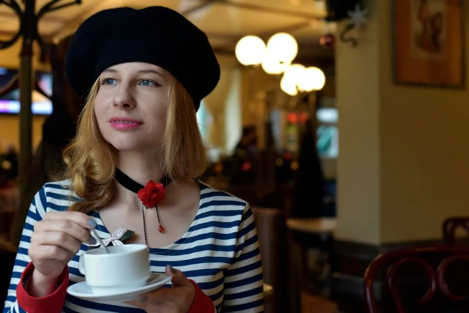 A woman in a striped top and beret enjoys coffee indoors, exuding Parisian style.