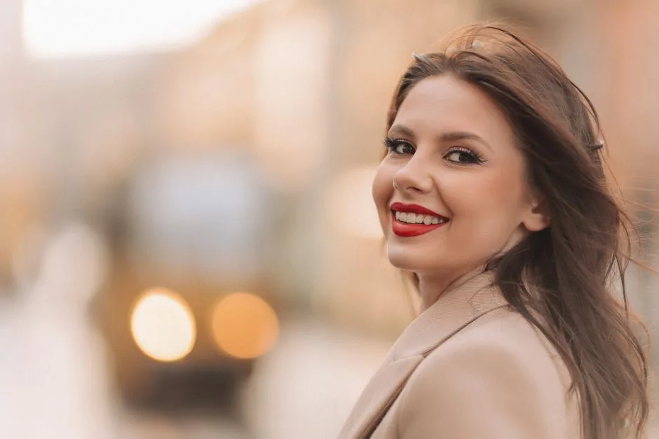 Portrait of a smiling woman with red lipstick and brown hair outdoors.