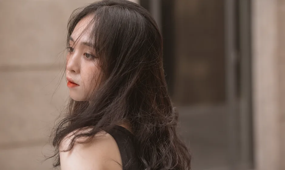 Close-up portrait of a young woman with long tousled hair in an urban setting.