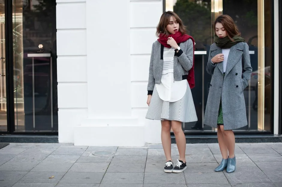 Two women showcasing stylish autumn coats and scarves against a city backdrop.