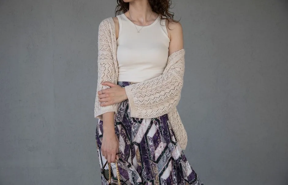 Elegant woman in a knitted cardigan and patterned skirt displaying modern fashion.