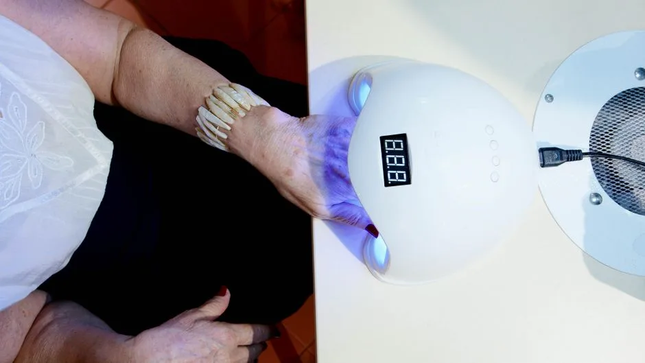 Close-up of a woman's hand with a bracelet using a nail dryer in a salon setting.