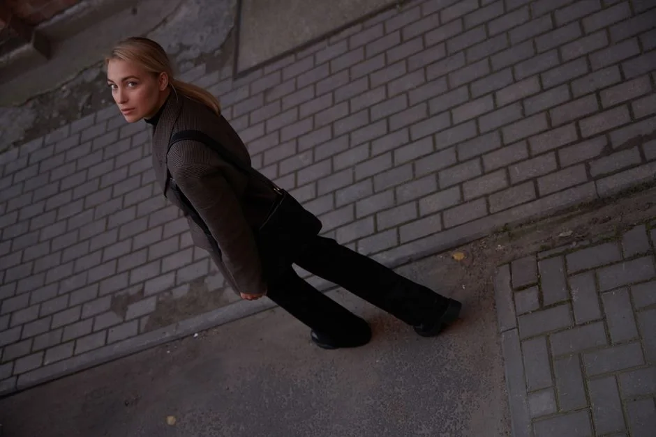 Woman in black clothing walking on a cobblestone street, looking over her shoulder.
