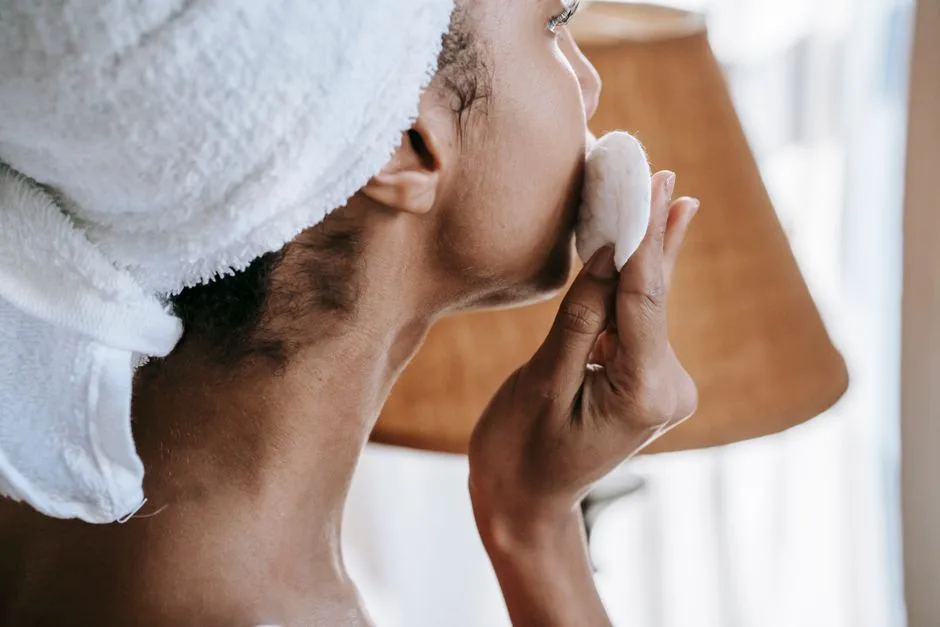 Side view of crop ethnic female in terry towel cleaning face with cotton disk at home in daylight