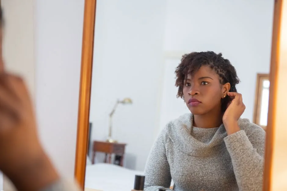 African American woman looking thoughtfully at her reflection indoors.