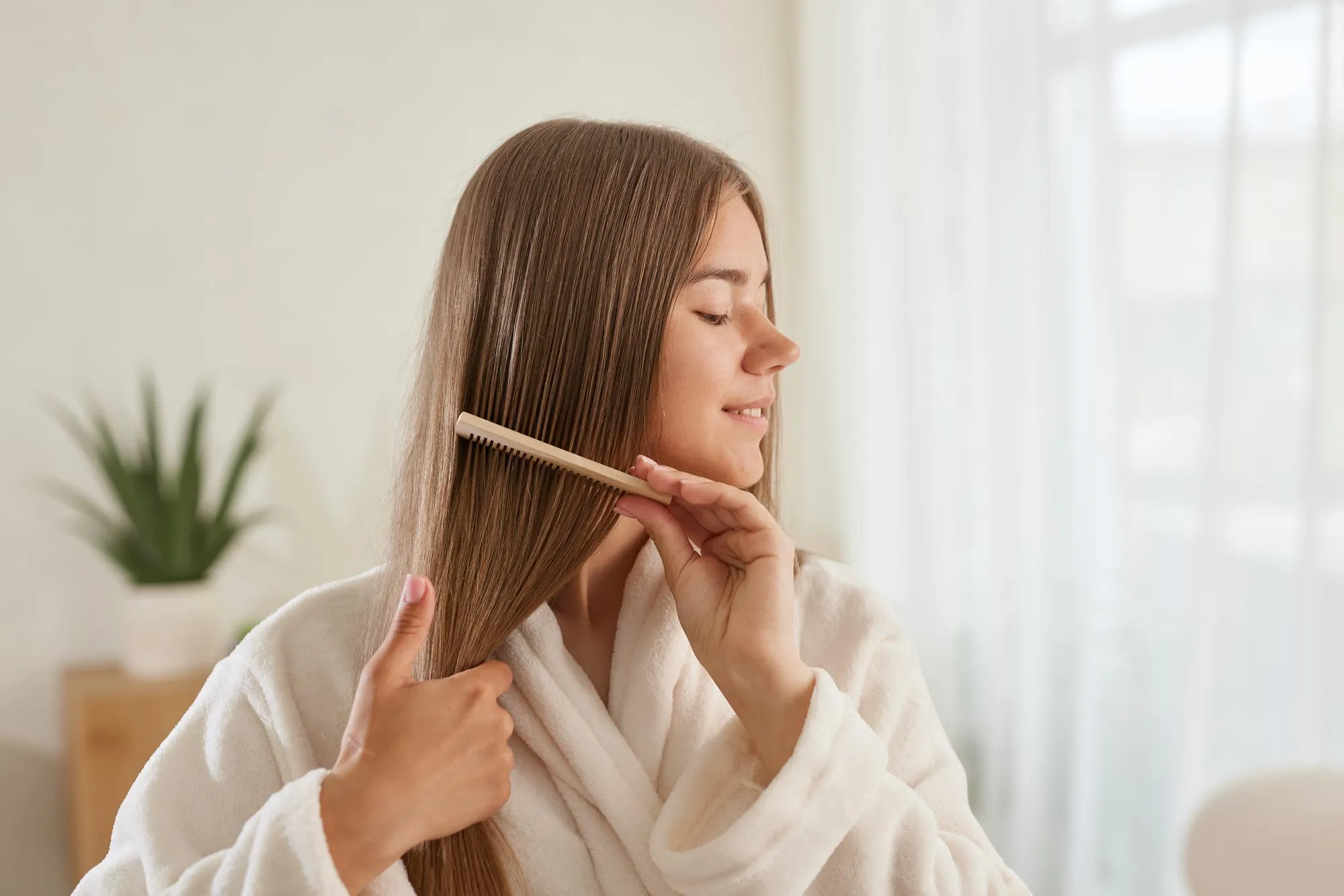 A young girl in a white coat takes care of her hair at home