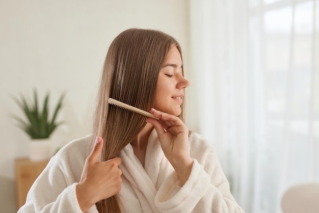 A young girl in a white coat takes care of her hair at home