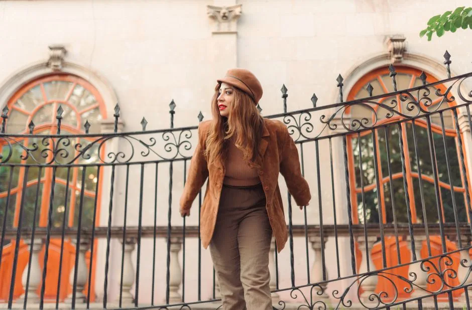 Stylish woman in autumn attire posing by ornate fence outdoors.