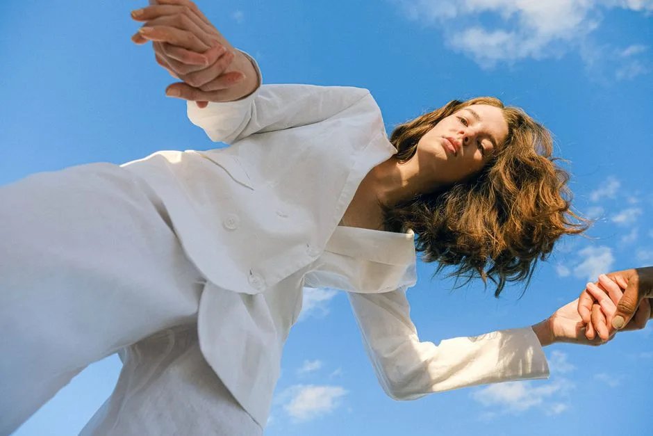 A woman in a white suit poses gracefully against a vibrant blue sky.