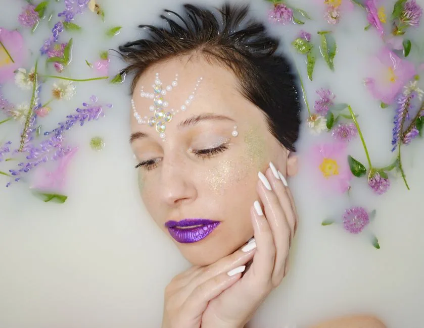 Top view of gentle female with purple lips and rhinestones on forehead lying in milk water with violet twigs during skincare procedure