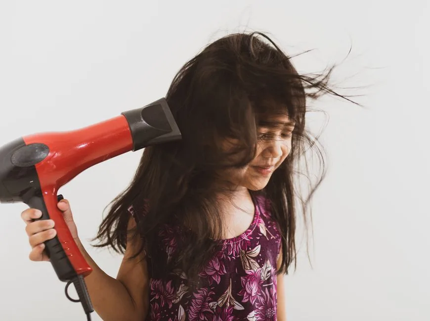 A happy girl using a hairdryer with her long hair blowing, indoors.