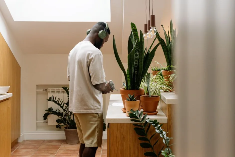 Relaxed man with headphones standing among indoor plants, enjoying music in a modern setting.