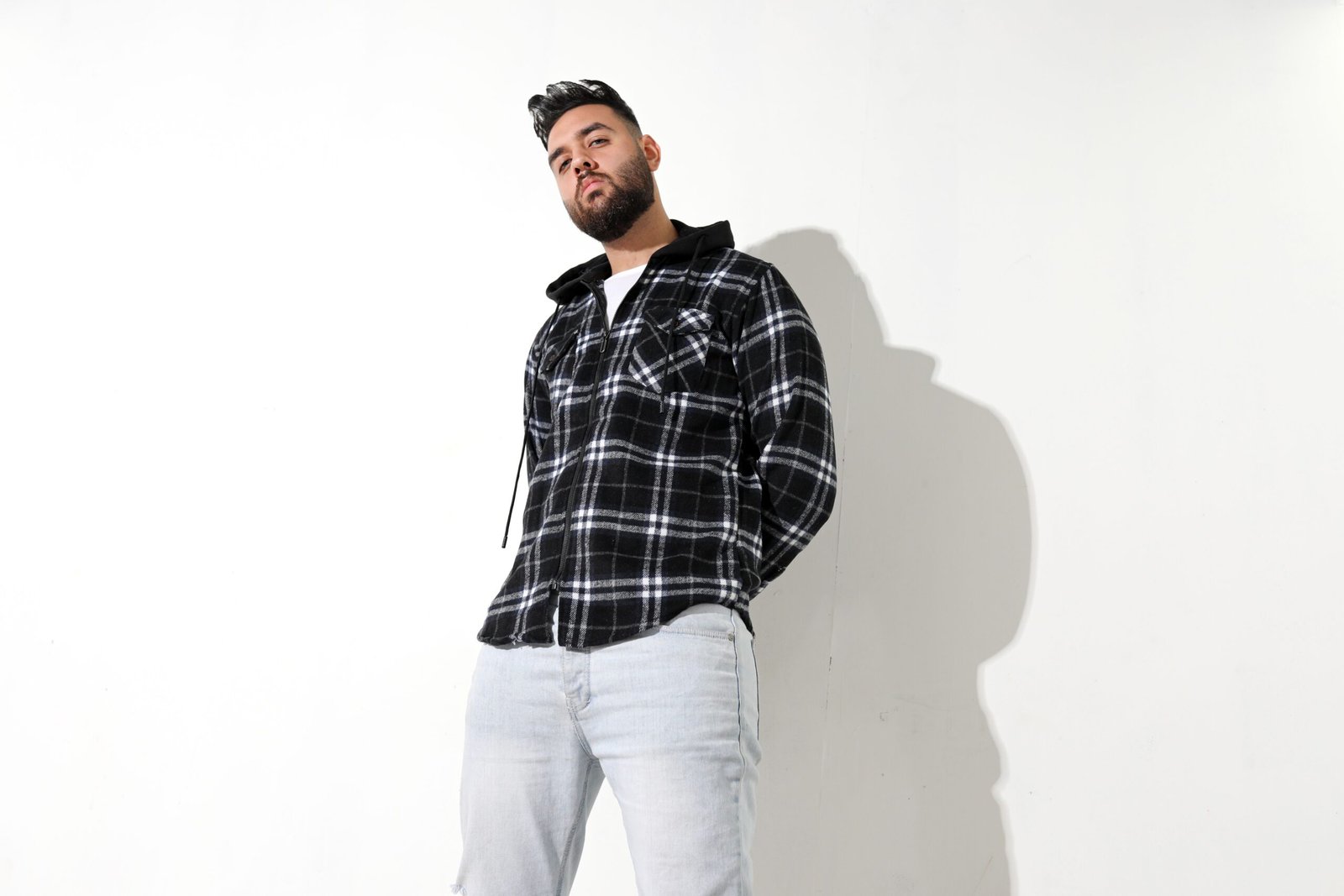 A stylish man in a plaid shirt poses confidently against a plain background, exuding a cool and casual vibe.