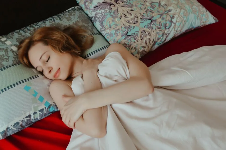 From above of relaxed female with arms crossed taking nap while lying on comfortable bed with pillows under blanket in bedroom