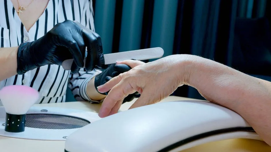 Close-up of a manicurist filing nails, providing professional salon service with gloves.