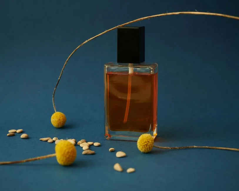 Elegant perfume bottle with yellow flowers and seeds on a blue background. Perfect for product mockups.