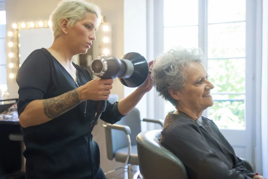 A skilled hair stylist blow drying a senior woman's hair in a modern salon.
