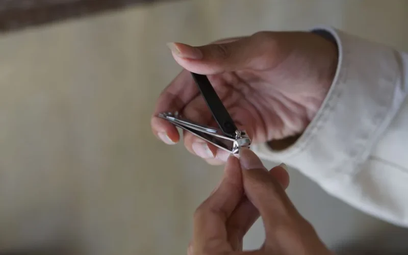 A person using a nail clipper to trim nails with focus on hand and clipper indoors.