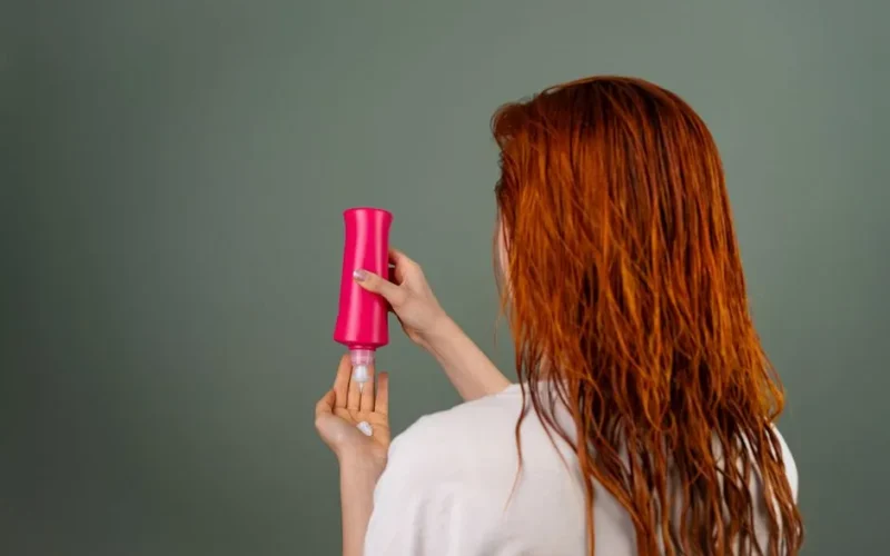 Adult woman with wet red hair applying conditioner. Hair care routine.