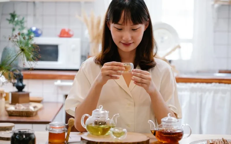A young woman savoring tea in a bright, cozy kitchen setting.