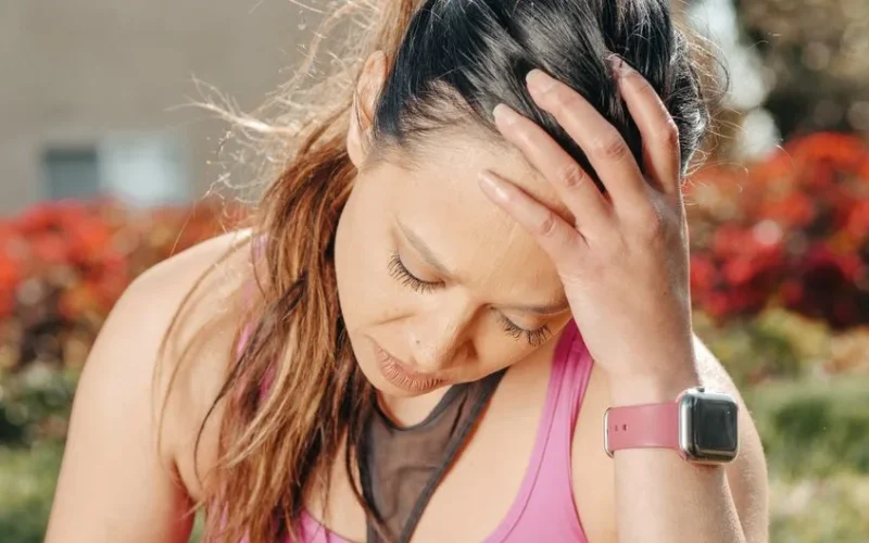 Close-up of a woman with a headache sitting outdoors wearing a smartwatch.