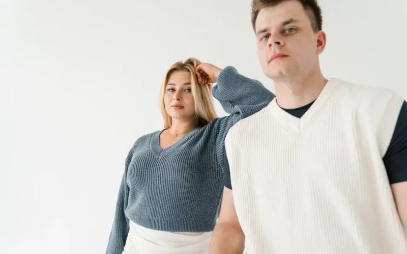 Two adults posing in a minimalist studio with stylish knitwear, showcasing fashion and confidence.