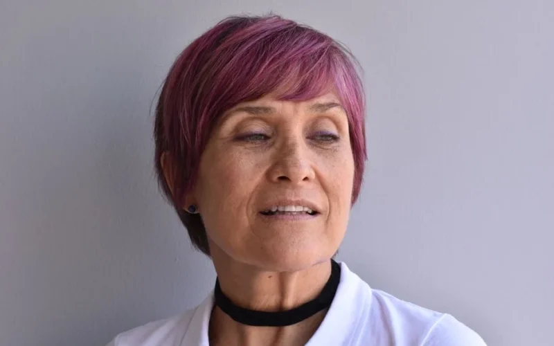 Close-up portrait of a woman with purple dyed hair and a black choker, looking thoughtful.