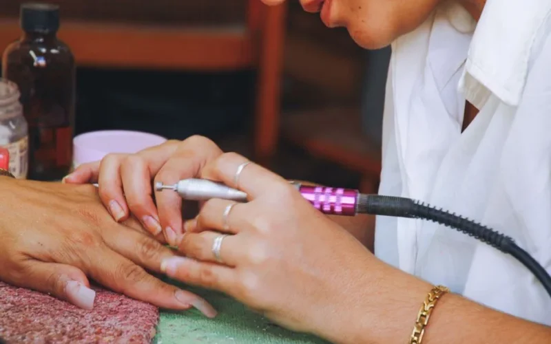Close-up image of a nail technician using an electric file on a client's nails during a manicure session.