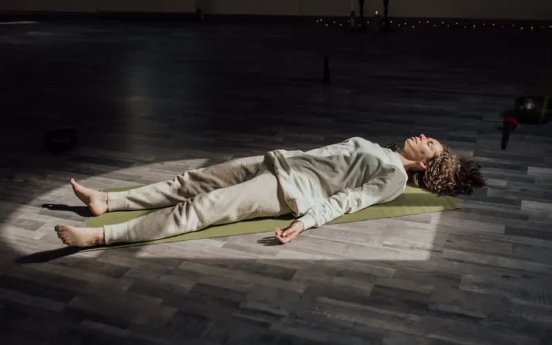 Woman lying on a yoga mat indoors, meditating and relaxing in a calm setting.