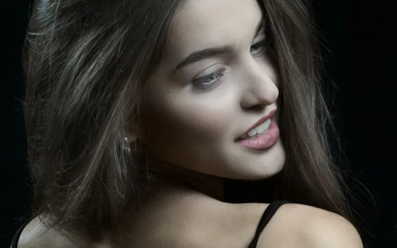Portrait of a woman with long brown hair posing confidently against a black background.