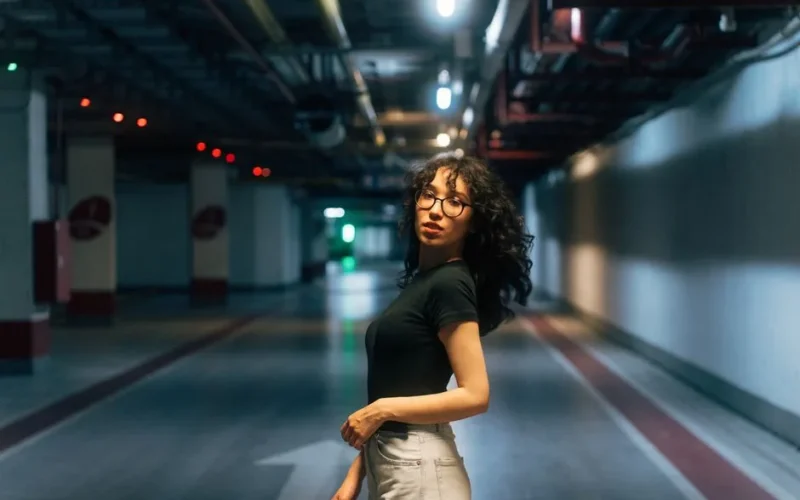 Fashionable woman with curly hair posing confidently in a well-lit underground tunnel.