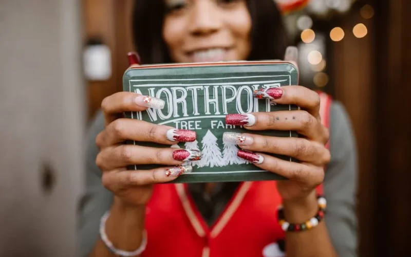 Smiling woman holding a Northpole gift tin with festive nail art, perfect for holiday themes.