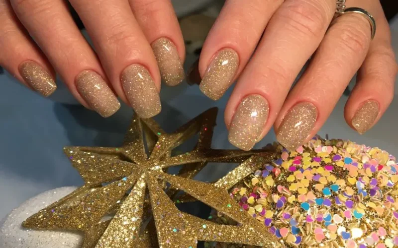 Elegant gold-glittered nails with star decorations, perfect for festive occasions.