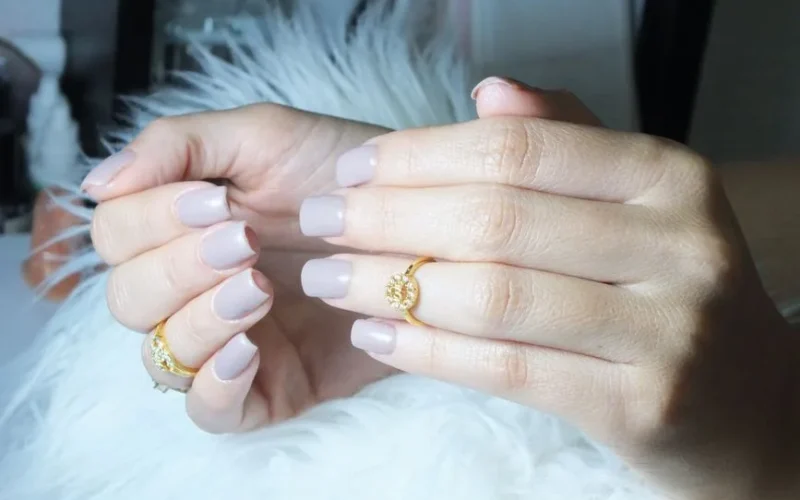 Close-up of beautiful manicured hands showcasing grey nails and gold rings in a serene setting.